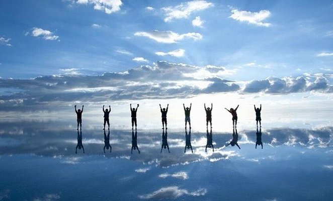 Viajantes reflectem na água durante a melhor altura para visitar o Salar de Uyuni